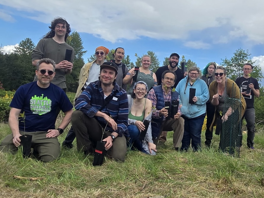 photo of a group of smiling students holding potted plants in a field