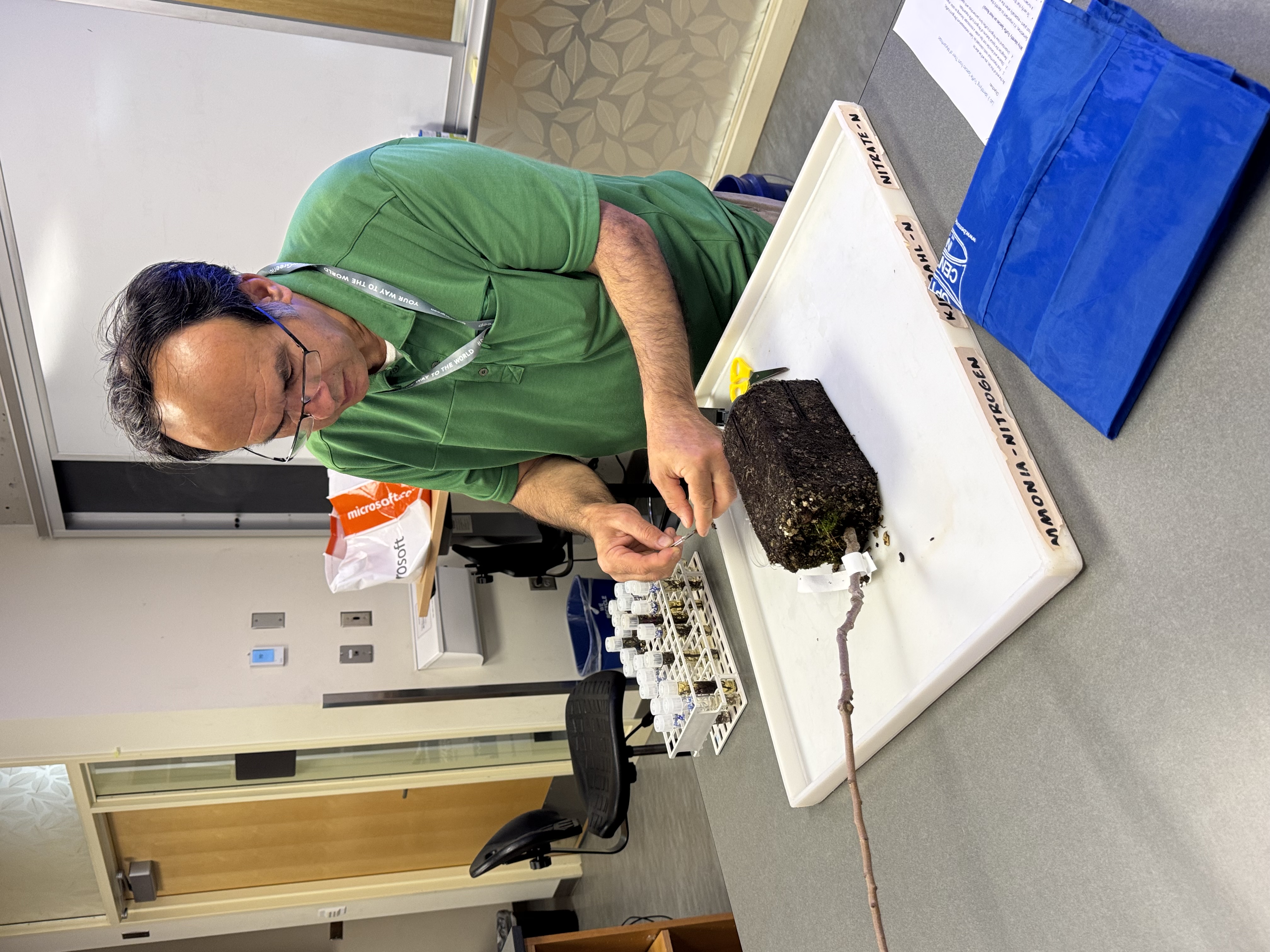 photo of a man in a green shirt in a labratory working with the roots of a potted plant