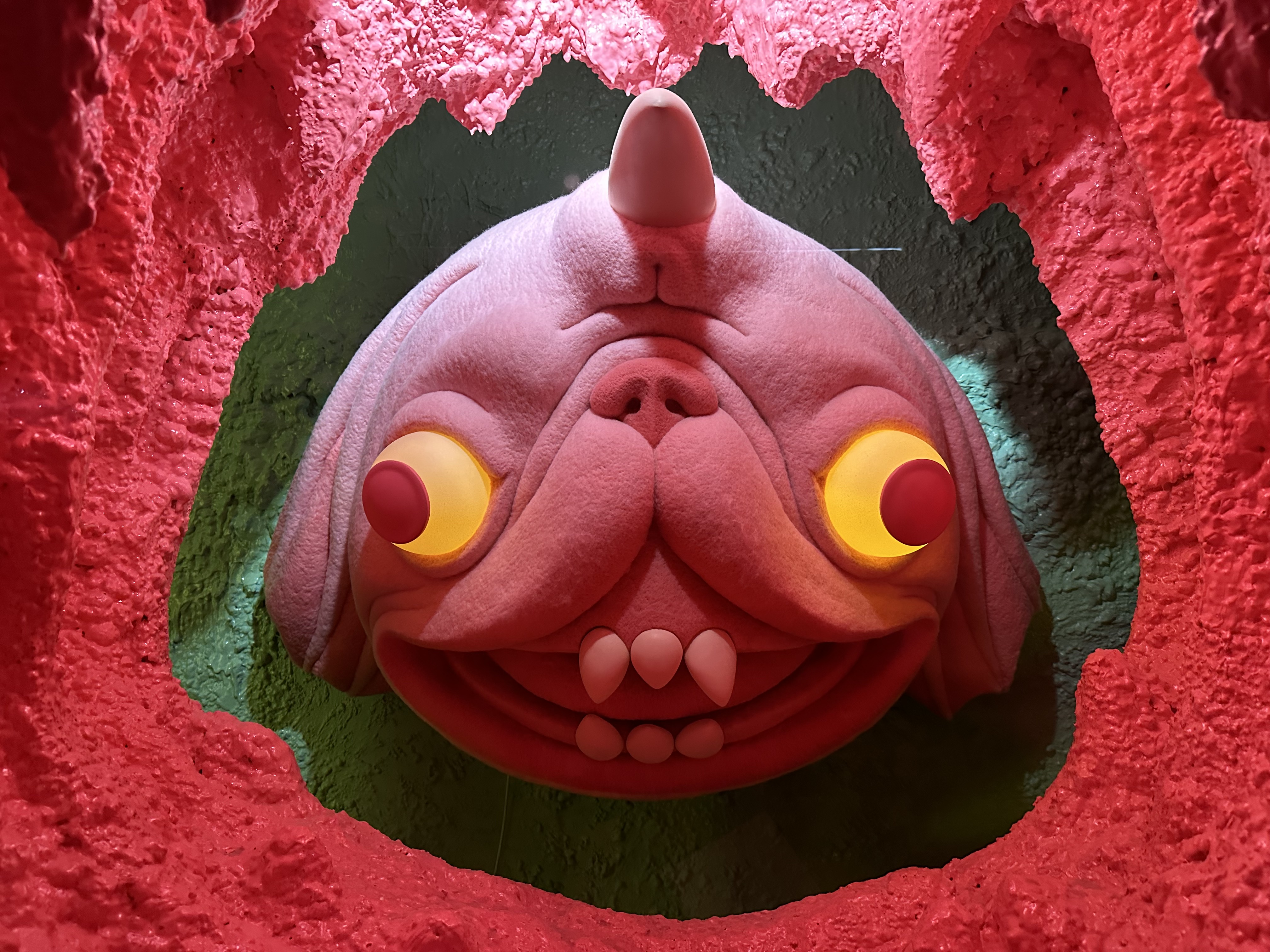 photo of a sculpture of a dog-like cartoon character with glowing yellow eyes and bubblegum pink fur